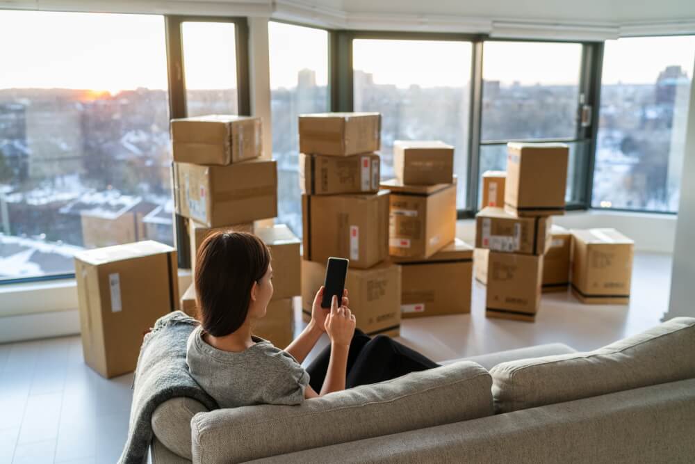 Femme assise sur son canapé à côté de son carton de déménagement.